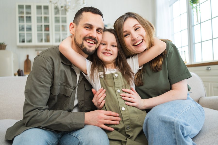 A family of three sitting close together and smiling.